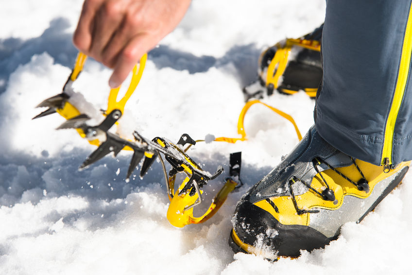 Ein Mann legt an seine steigeisenfesten Wanderschuhe Steigeisen an