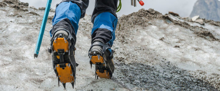 Ein Bergsteiger trägt Gamaschen während er mit Steigeisen über einen Gletscher läuft